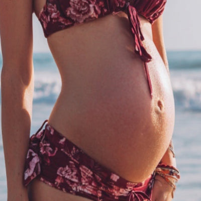 Women standing on beach with pregnant belly showing